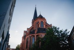 Rote Backsteinkirche St. Nicolai in Lüneburg mit spitzem Turm unter blauem Himmel.