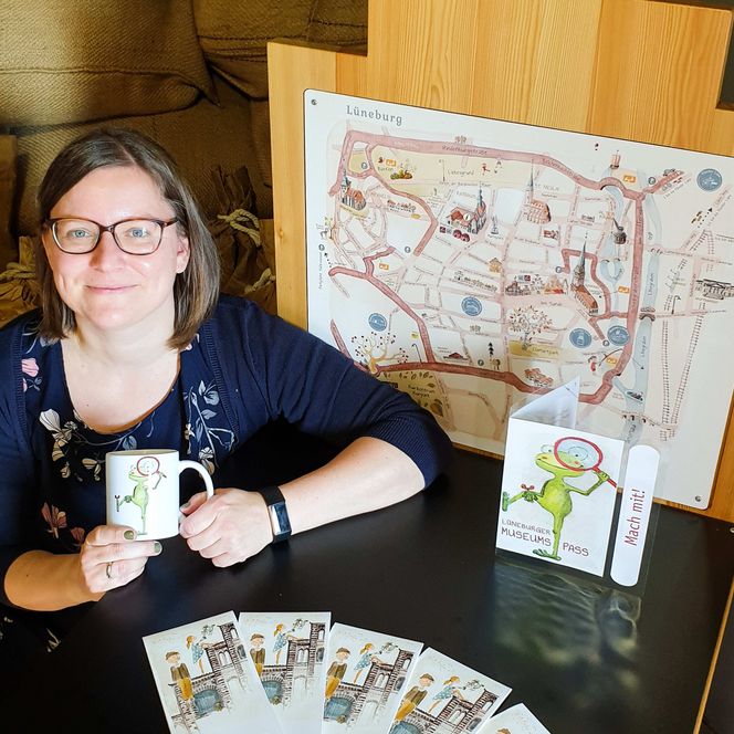 Ein Frau hockt neben einem sogenannten Giebeltisch im Salzmuseum Lüneburg und hält ihre Rätselkarte hoch. Auf dem Tisch liegen Stadtpläne.