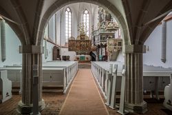 Blick durch Steinbögen auf weiße Bänke und den verzierten Altar im Kloster Lüne.