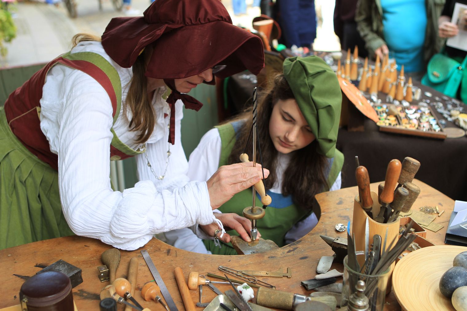 Zwei Frauen in historischer Gewandung fertigen Handwerkskunst an einer Werkbank.