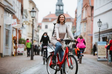 Eine Frau fährt auf einem Fahrrad, dem sogenannten StadtRAD, durch eine Straße in der Innenstadt Lüneburgs.