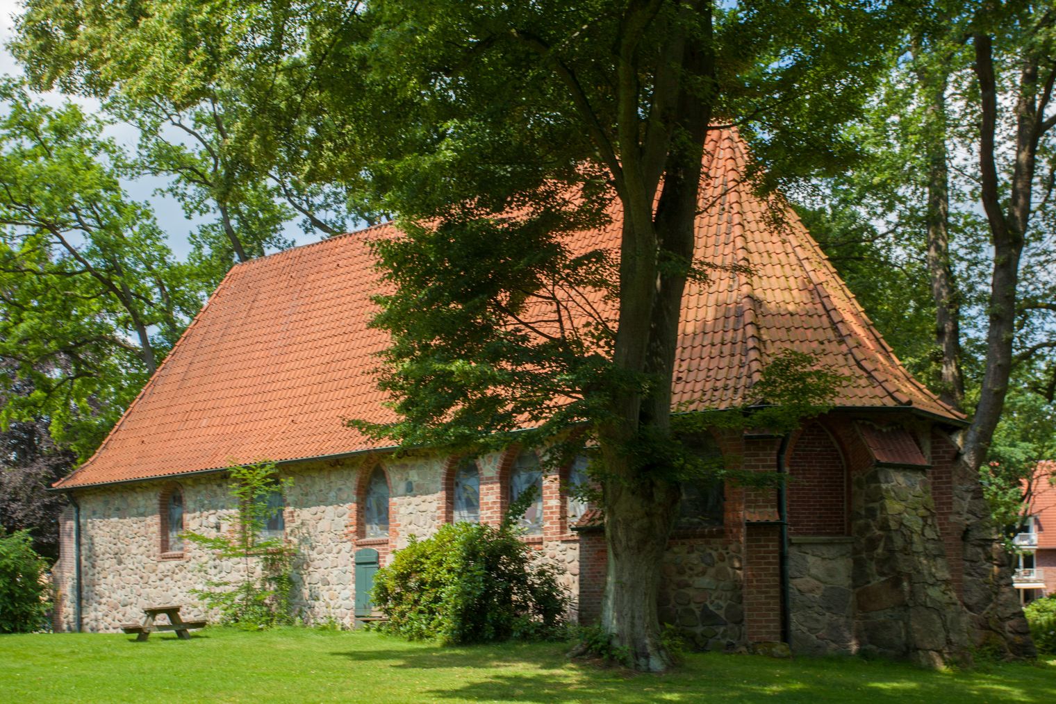 Die alte Kirche in Bispingen aus Feld- und Backsteinen mit rotgedecktem Satteldach, umgeben von Grün.