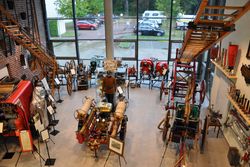 Helle Museumshalle mit historischen Feuerwehrwagen, hölzernen Leitern, Pumpen und alten Uniformen.